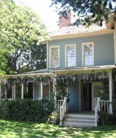 a blue house with white trim and flowers on the front porch is surrounded by greenery