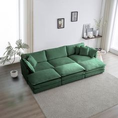 a large green couch sitting on top of a wooden floor next to a plant in a living room