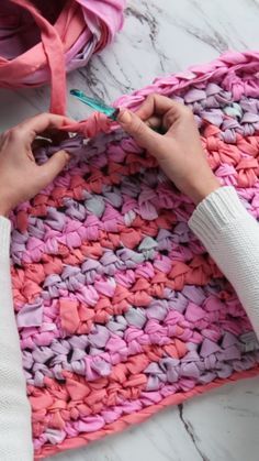 a woman is crocheting a pink and purple afghan on the floor with scissors