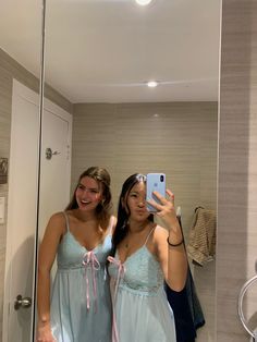 two women in blue dresses taking a selfie in front of a mirror with their cell phone