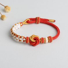 a red and white bracelet with gold accents on a white table next to dried flowers