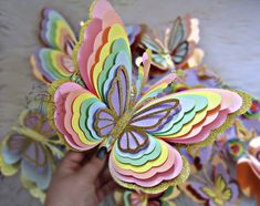 a hand holding a colorful paper butterfly on top of a white wall with butterflies in the background