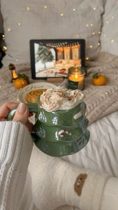 a person holding a mug in front of a bed with oranges and candles on it