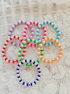 four bracelets with different colored beads on a lace tablecloth, one is white and the other is multicolored