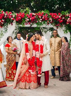 the bride and groom are standing under an arch decorated with red flowers for their wedding ceremony