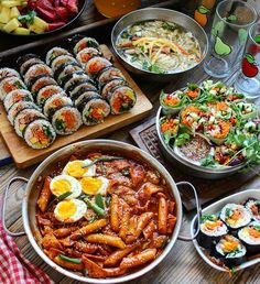 an assortment of sushi and other food items on a wooden table with plates, bowls, glasses and utensils