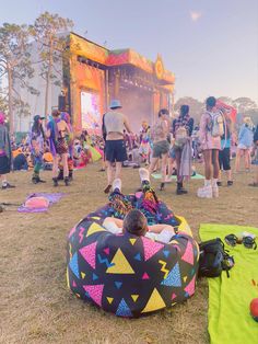 a group of people standing and sitting on top of a grass covered field next to a stage