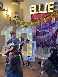 a young boy playing guitar in front of a group of people sitting on the floor