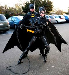 two people dressed up as batman and batgirl in a parking lot with cars behind them