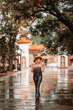 a woman is walking down the street in the rain with an umbrella and red hat