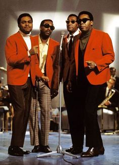 three men standing next to each other in front of a microphone and wearing red suits