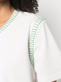 a woman with curly hair wearing a white t - shirt and green trimmings