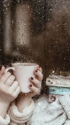 a woman holding a coffee cup in front of a window covered with raindrops