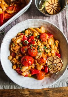 pasta with tomatoes and chickpeas in a white bowl next to other food items