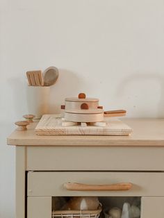 a wooden table topped with pots and pans on top of a white dresser next to a wall