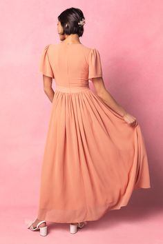 a woman in an orange dress is standing against a pink background with her back to the camera