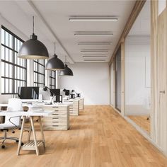 an empty office with wooden floors and black hanging lamps above the desks, along with two computer monitors