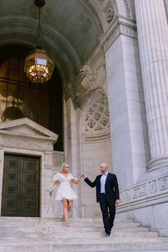 a bride and groom walking down the steps of an old building with columns on either side