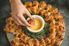 a person dipping something into a small bowl on top of pigs in a blanket with rosemary sprigs