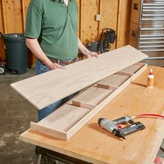 a man standing in front of a workbench holding a piece of plywood