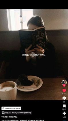 a woman sitting at a table reading a book and drinking coffee in front of her