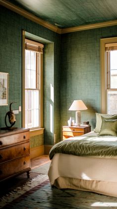 a bed sitting in a bedroom next to two windows and a lamp on top of a dresser