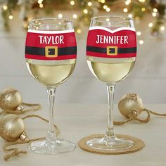 two wine glasses with santa's hat and name on them sitting next to christmas decorations