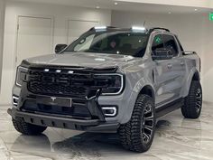 a silver truck is parked in a large room with white walls and floor tiles on it