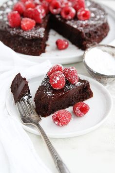 a chocolate cake with raspberries and powdered sugar on the plate next to it