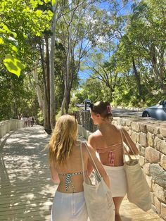 two women in bathing suits walking down a sidewalk with bags on their backs and one carrying a bag