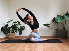 a woman is doing yoga on a mat in the middle of a room with potted plants