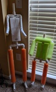 three orange and green candles sitting in front of a window next to a toilet paper dispenser