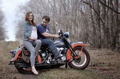 a man and woman riding on the back of an orange motorcycle in a wooded area