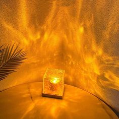 a lit candle sitting on top of a round table next to a plant and wall