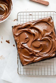 a chocolate frosted cake on a cooling rack next to a bowl of melted chocolate