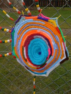 a multicolored piece of art hanging on a chain link fence in the yard