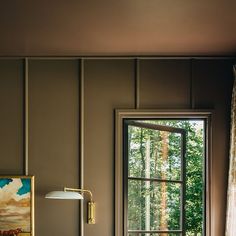 a bed sitting under a window next to a lamp on top of a wooden table