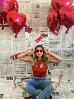 a woman sitting on top of a stool in front of some red heart shaped balloons