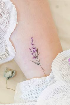 a small lavender flower tattoo on the side of a woman's leg and ankle