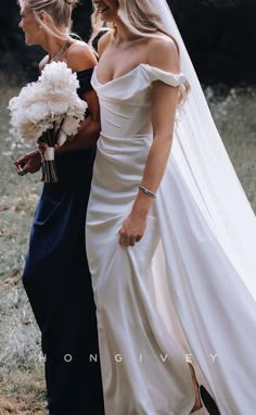 two women in wedding gowns are walking side by side with one holding a bouquet