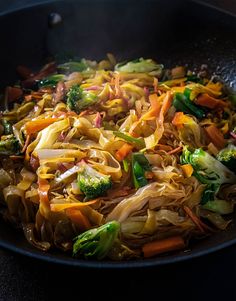 a wok filled with noodles and vegetables on top of a table