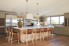 a large kitchen with an island and wooden chairs in the center, surrounded by windows