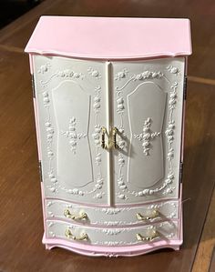 a pink and white cabinet sitting on top of a wooden table