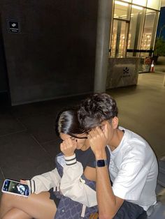 a man and woman sitting on the ground looking at their cell phones