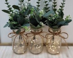 three glass vases with flowers and greenery in them