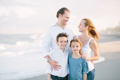 a family standing on the beach with their arms around each other and smiling at the camera