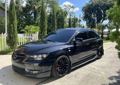 a black car parked in front of a white fence and some trees on the street