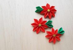 three red and green paper flowers sitting on top of a wooden table