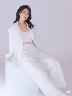 a woman sitting on top of a chair wearing white pants and a blazer jacket