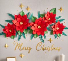 a christmas card with paper poinsettis and gold lettering on a grey background